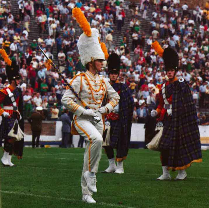 A woman in a white drum major outfit on the football field with the Irish Guard.