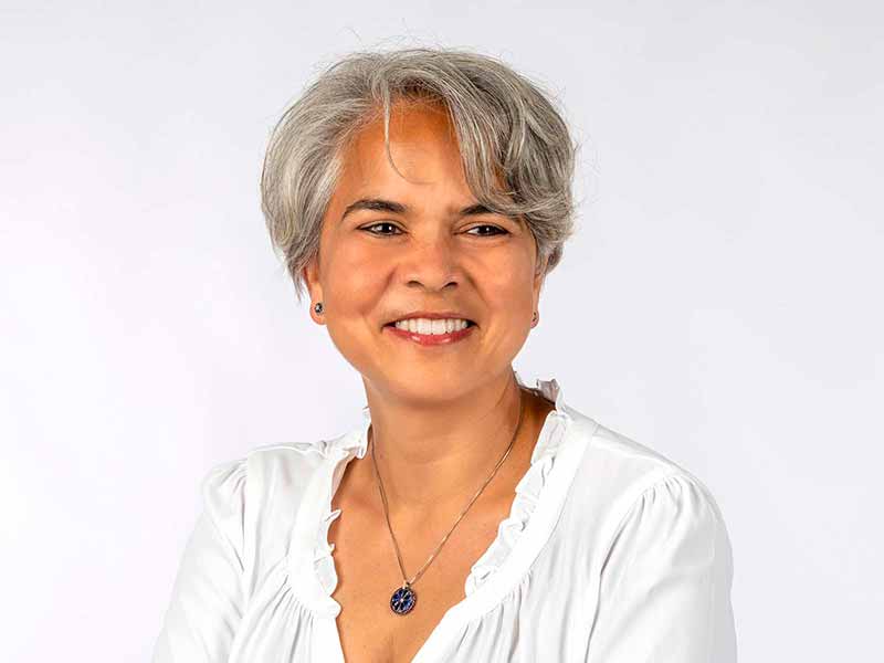A portrait of a woman with short salt and pepper hair smiling and looking to the side of the camera.