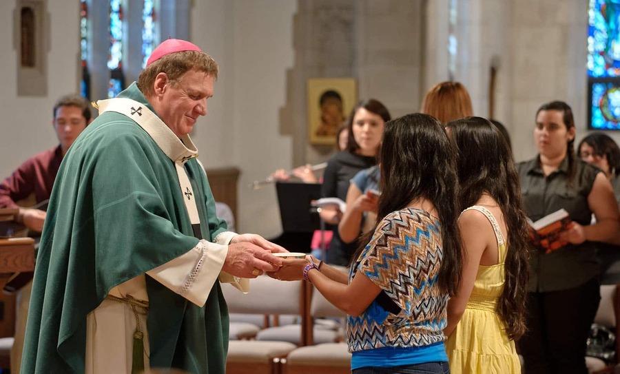A female student grabs a bowl from a priest during Mass.
