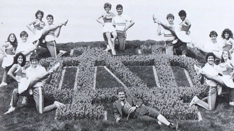 A cheer squad pose around an ND monogram bush sculpture.