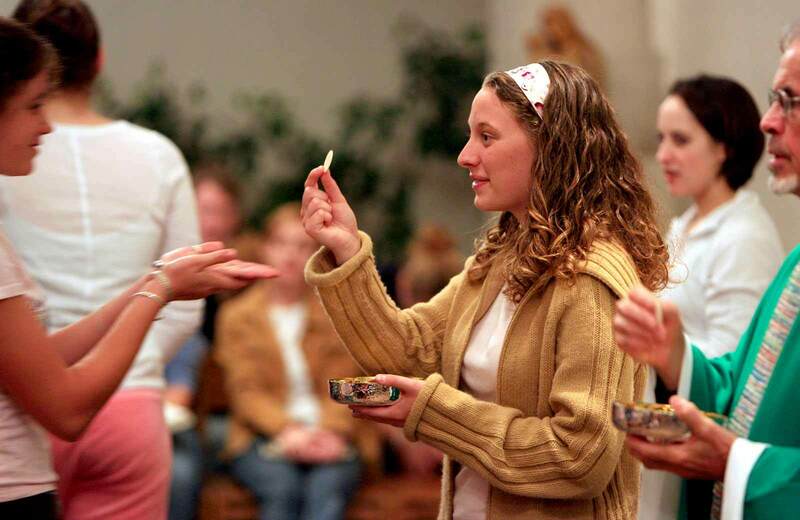 A female student holds up a wafer, giving communion during mass.