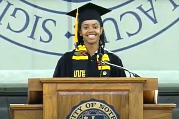 A black female student in graduation cap and gown smiles at a graduation podium.