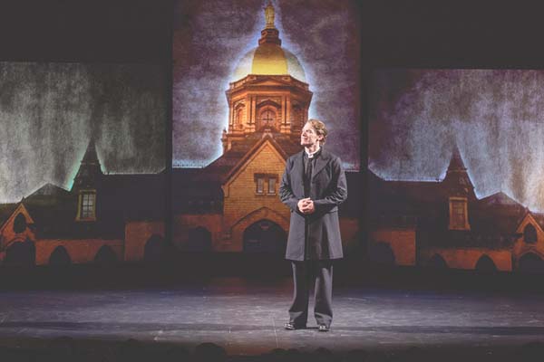 An actor portraying Fr. Sorin on stage in front of a Golden Dome backdrop.